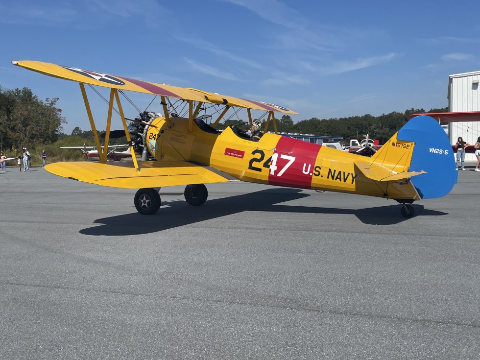 A vintage yellow biplane with red and blue accents, marked 'U.S. Navy 247', sits on a tarmac in Suwannee County, Florida.