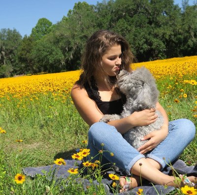 Author Hayli Zuccola sitting with her dog in a field of flowers