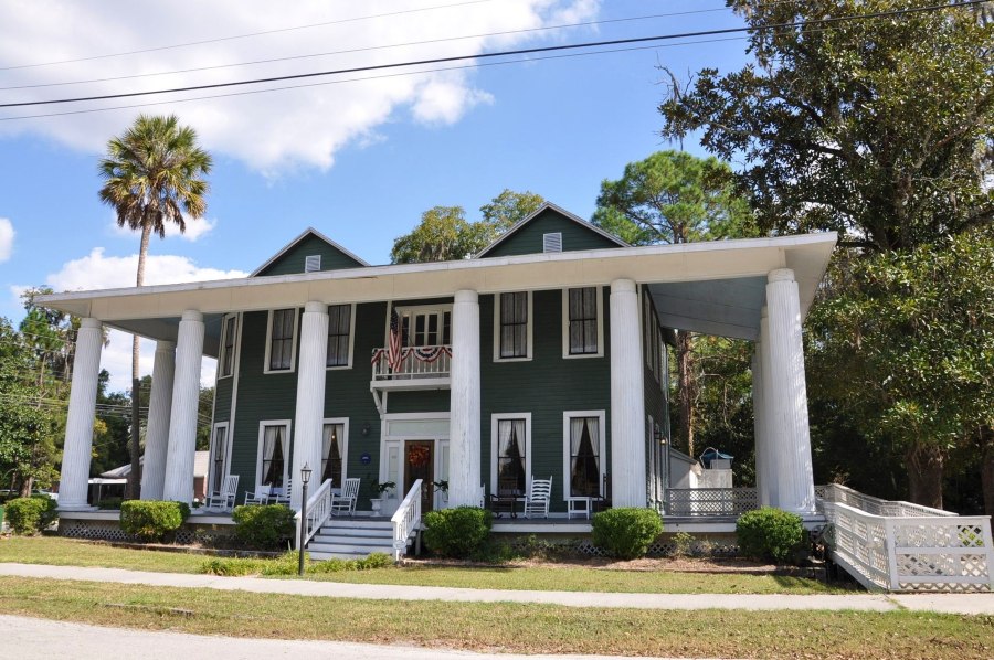 The stately facade of The 406 restaurant shows white pillars and surrounding vegetation, at this local Live Oak restaurant and bourbon bar.