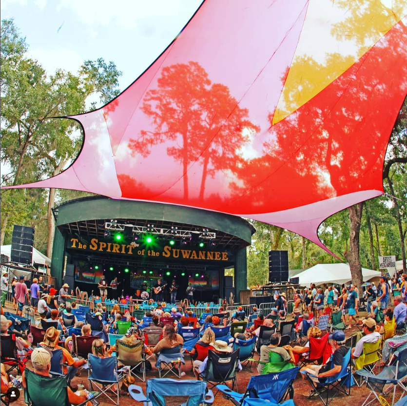 Festival-goers sit beneath a bright red canopy enjoying a live music set at Suwannee Roots festival held at Spirit of Suwannee Music Park.