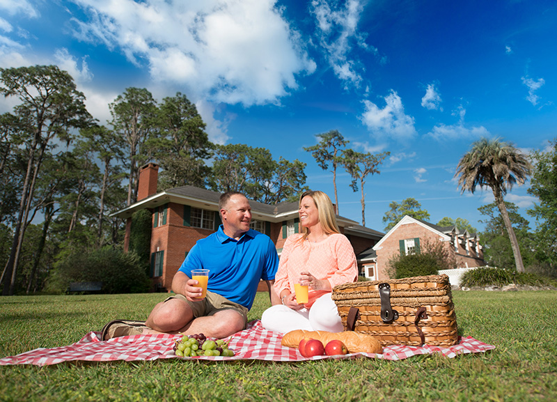 A couple sits on a red checkered blanket enjoying a picnic basket filled with food in Suwannee County, Florida.