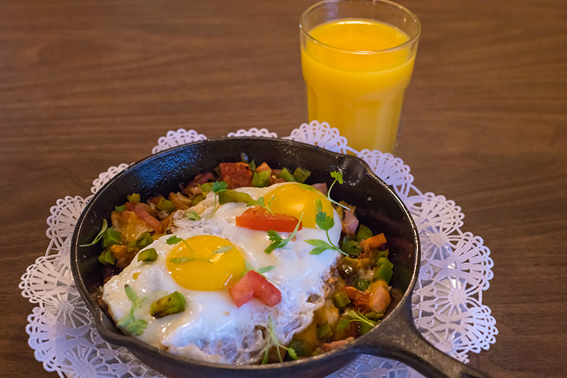 A skillet of hash and sunny-side-up eggs rests on a plate with a glass of orange juice from a local restaurant in Suwannee County, Florida.