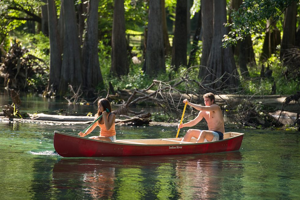 A young couple canoes down a waterway surrounded by trees in Live Oak within Suwannee County, Florida.